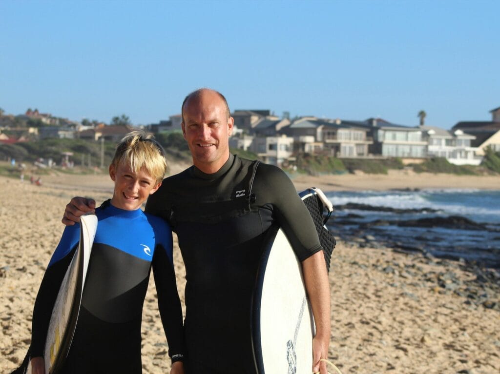 Dad and son in wetsuits with surfboards at beach for dad birthday ideas