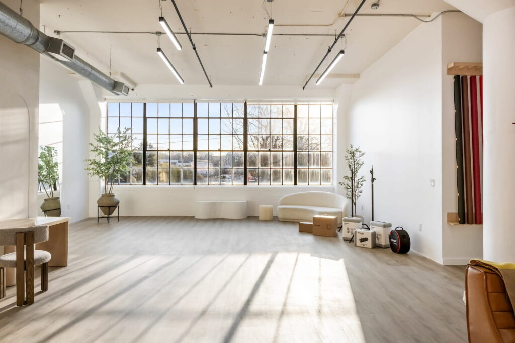 Softly-lit natural light photo studio with a large paned window and neutral-colored furniture