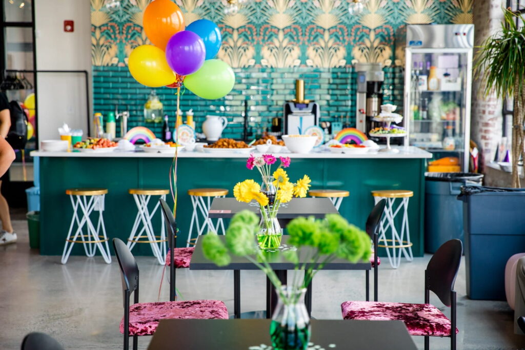 A Nashville gathering space is decorated with brightly-colored balloons and flowers and different appetizers atop a large green island