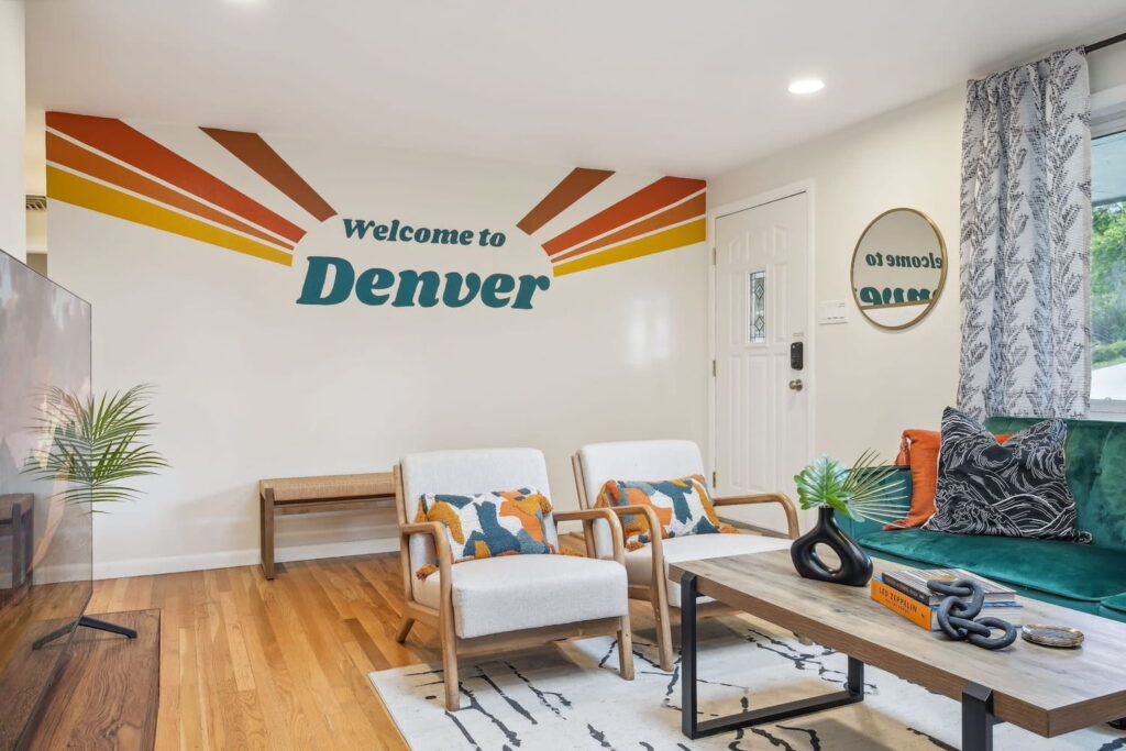 A small living room with aqua couch and bright pillows and a colorful Welcome to Denver mural on the wall