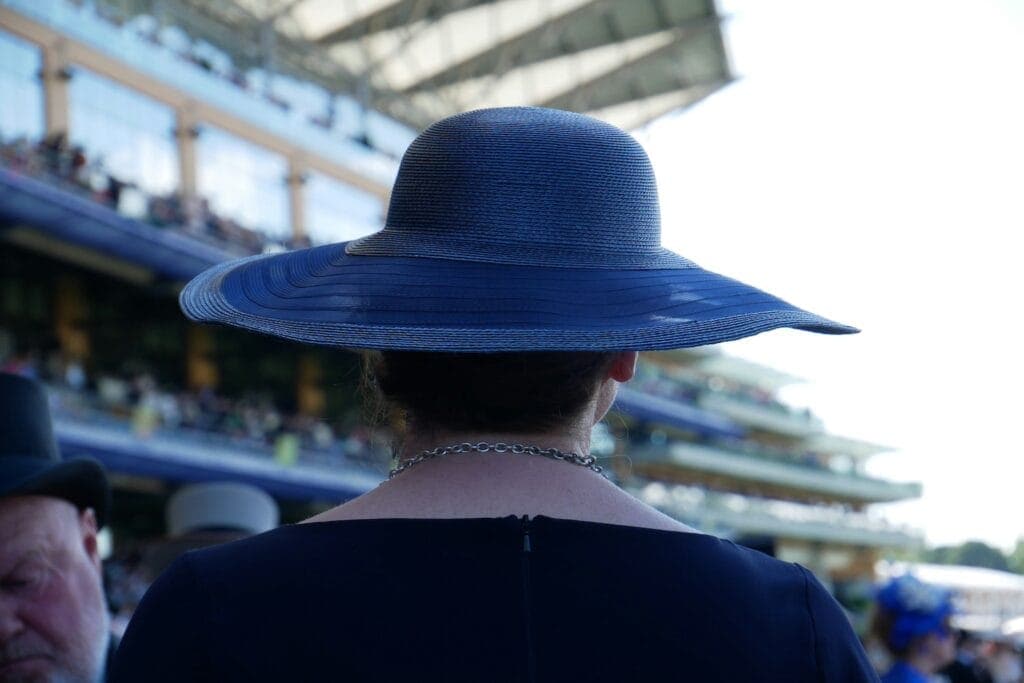 A woman wears a blue hat in the grandstand of a race
