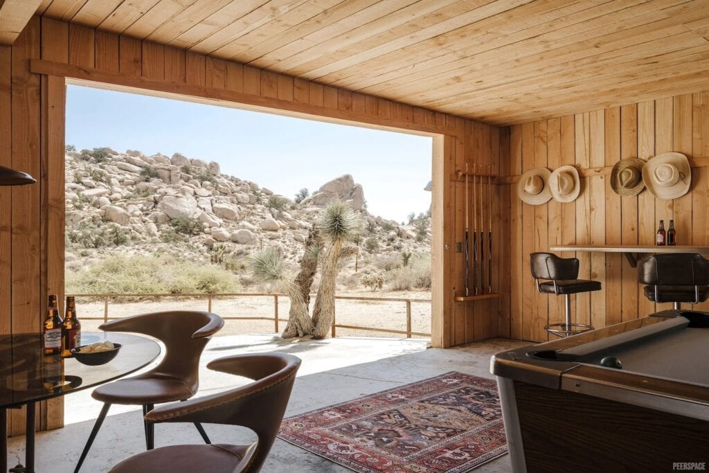 Western-inspired room with pool table, cowboy hats and captains chairs with a view of desert outside large doorway