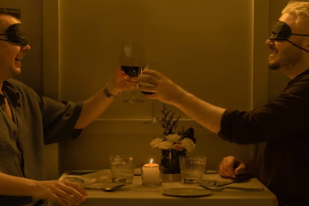 Two blindfolded men toast across a small dinner table at a Dining in the Dark event