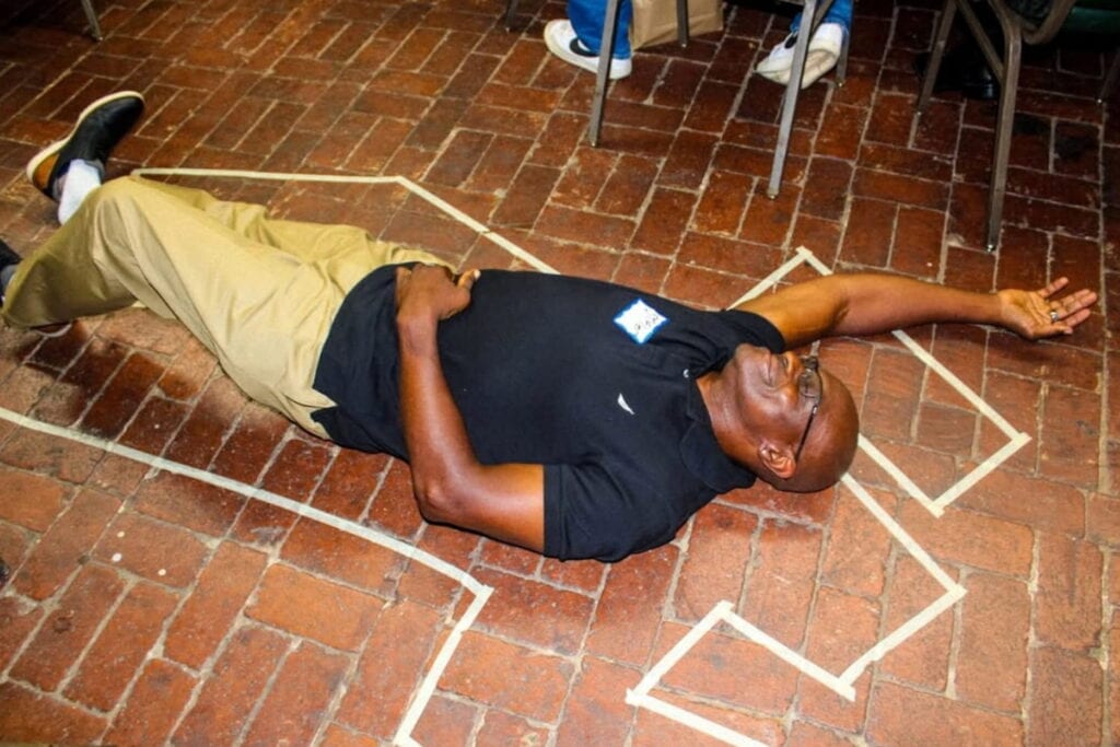 A participant in a dinner detective event lays on the floor inside of a chalk outline