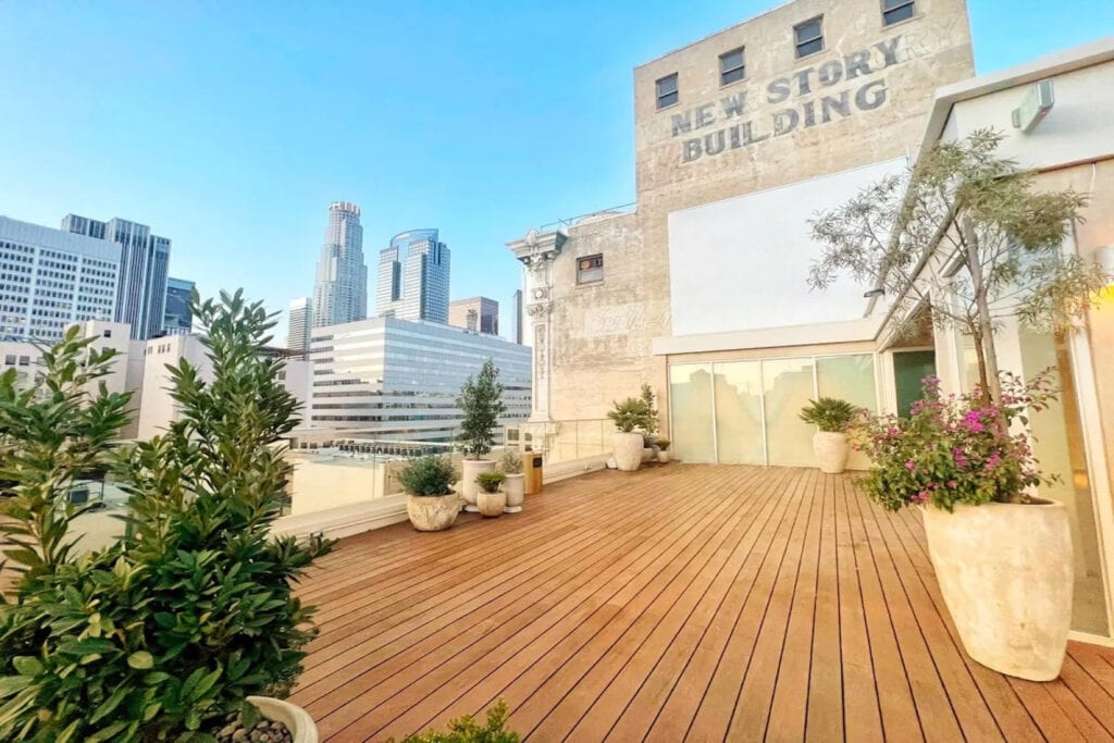 A large rooftop with potted trees and plants next to a brick building has downtown views of a city