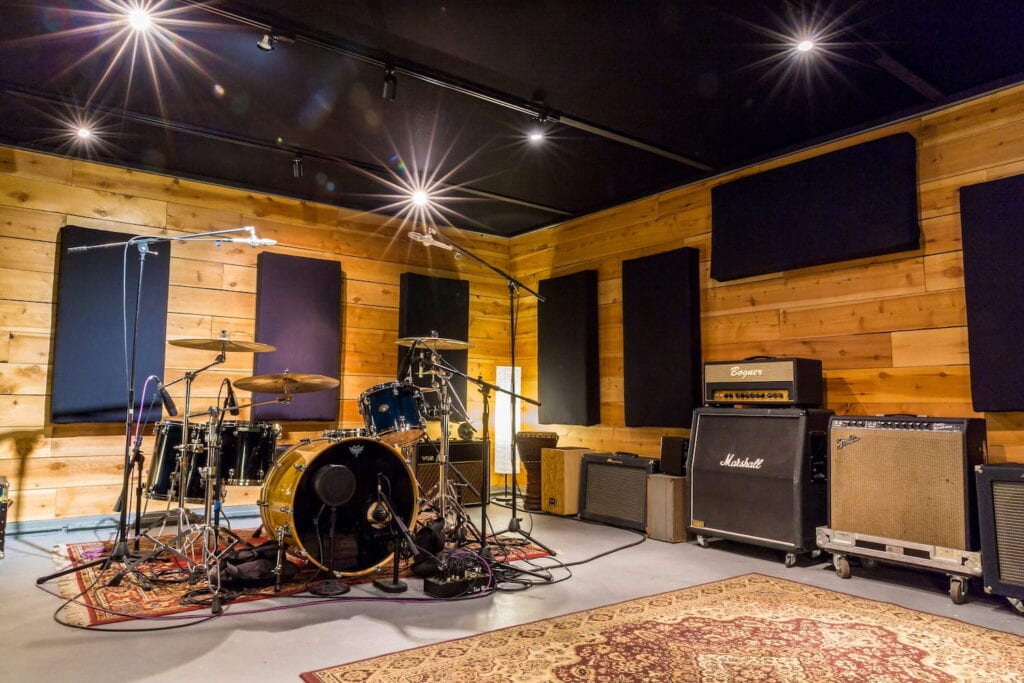 A guitar kit is illuminated by track lights in a warm studio with wooden shiplap walls