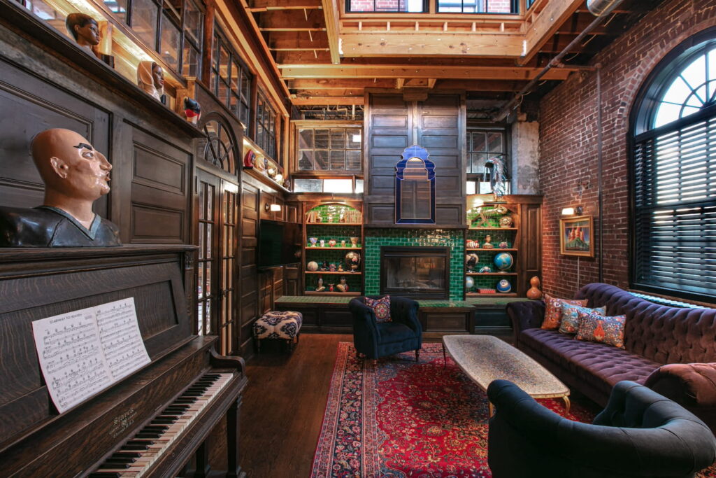 An eclectic, bohemian-style loft space with a deep, purple velvet couch, green-tiled firelplace and wooden accents