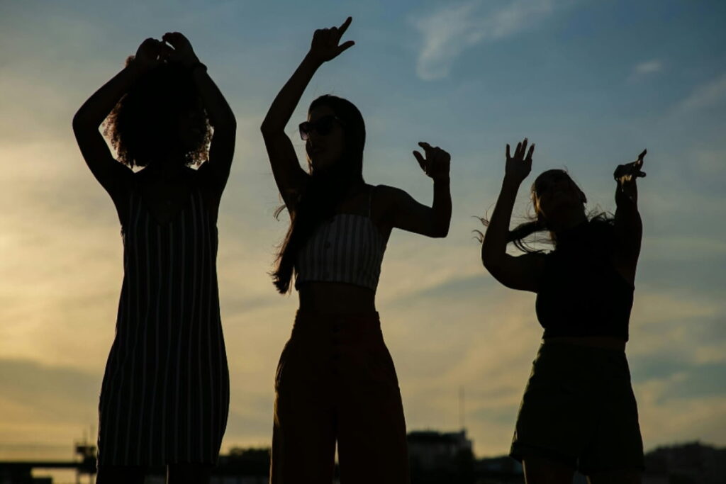 Silhouettes of three women dancing against a dimly-lit sky