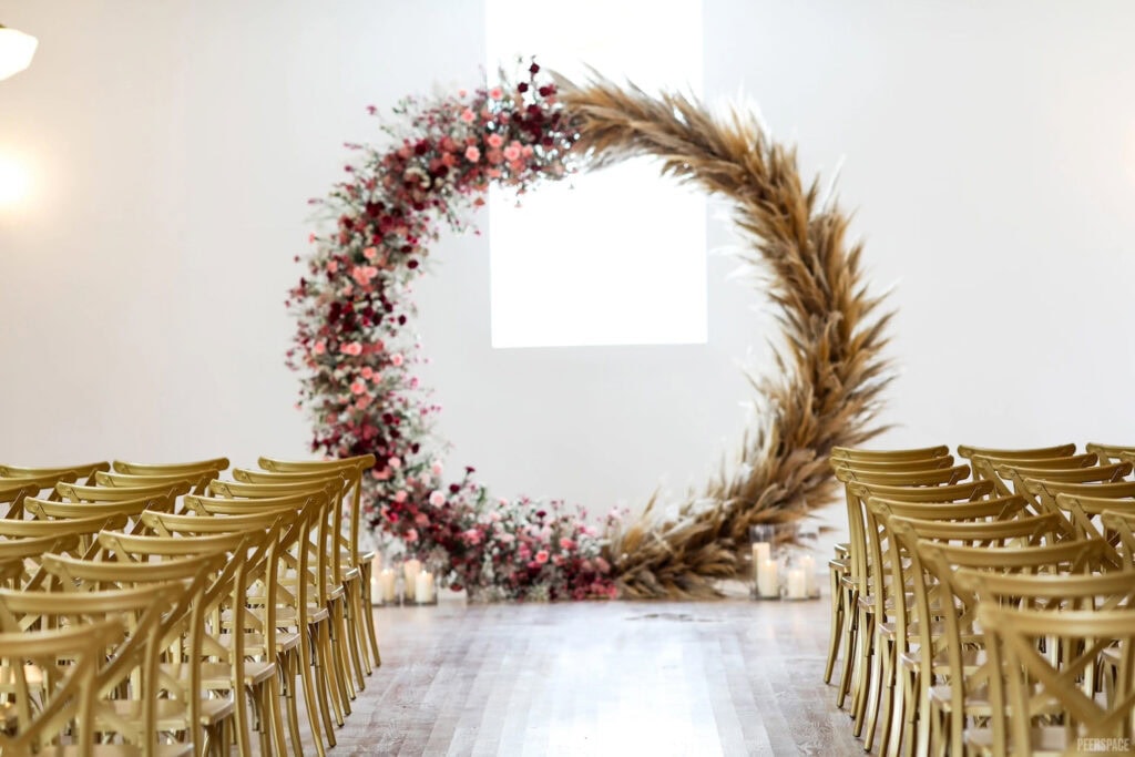 Wooden chairs line the aisle at a bright white wedding venue with a rustic wreath as the backdrop at the altar