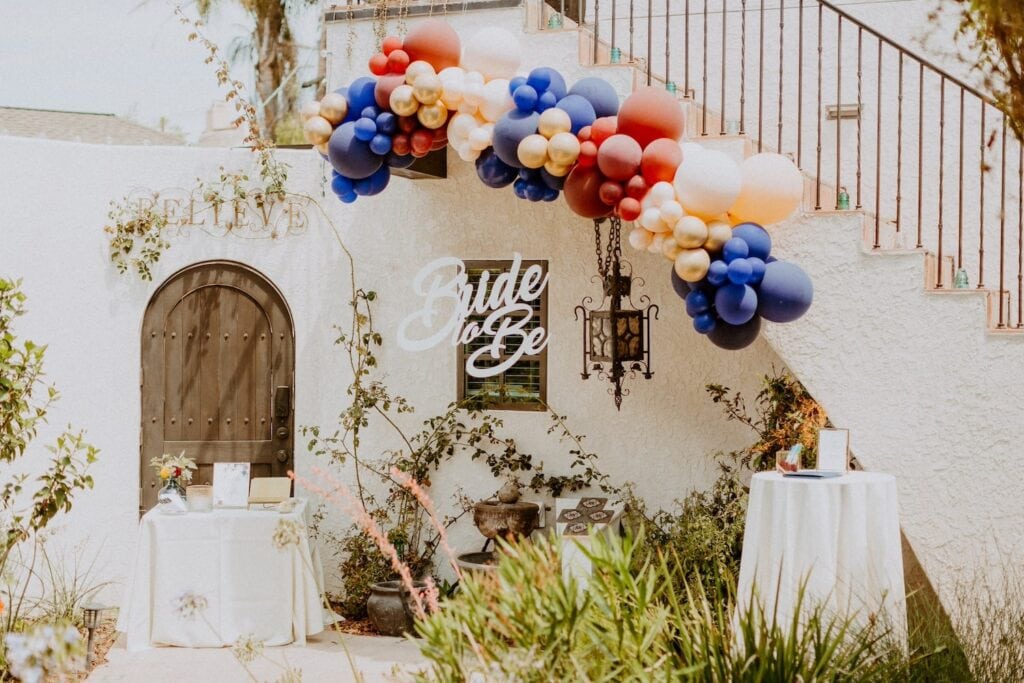 Balloons and a Bride to Be sign are set up outside of a beautiful stucco under a curved staircase