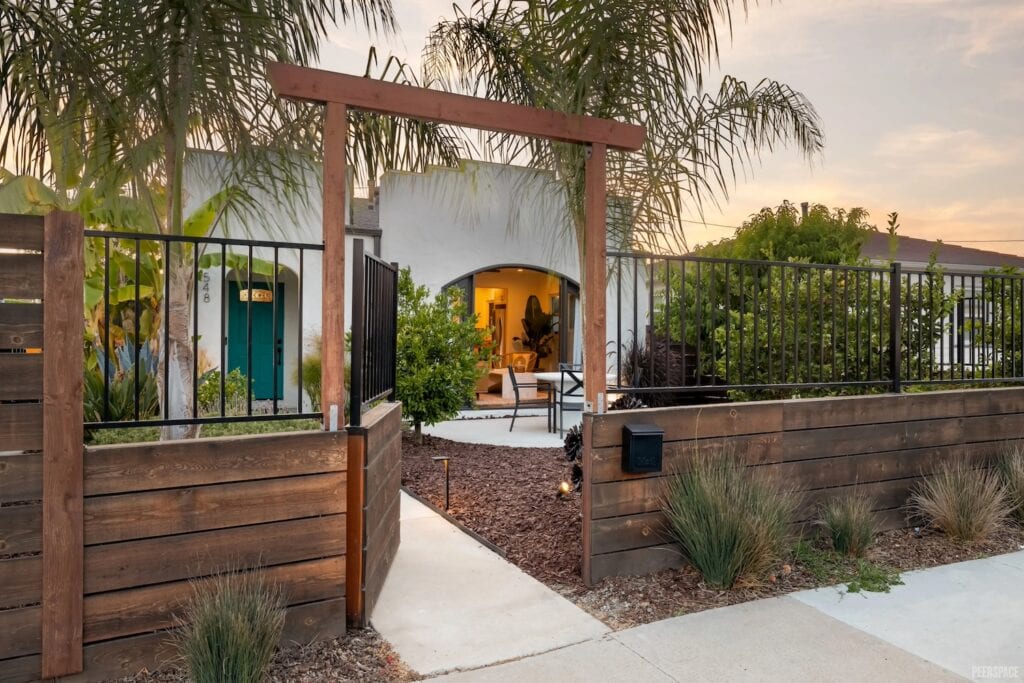 A wooden gate flanked by palm trees opens up to front yard of Spanish-style home in San Diego
