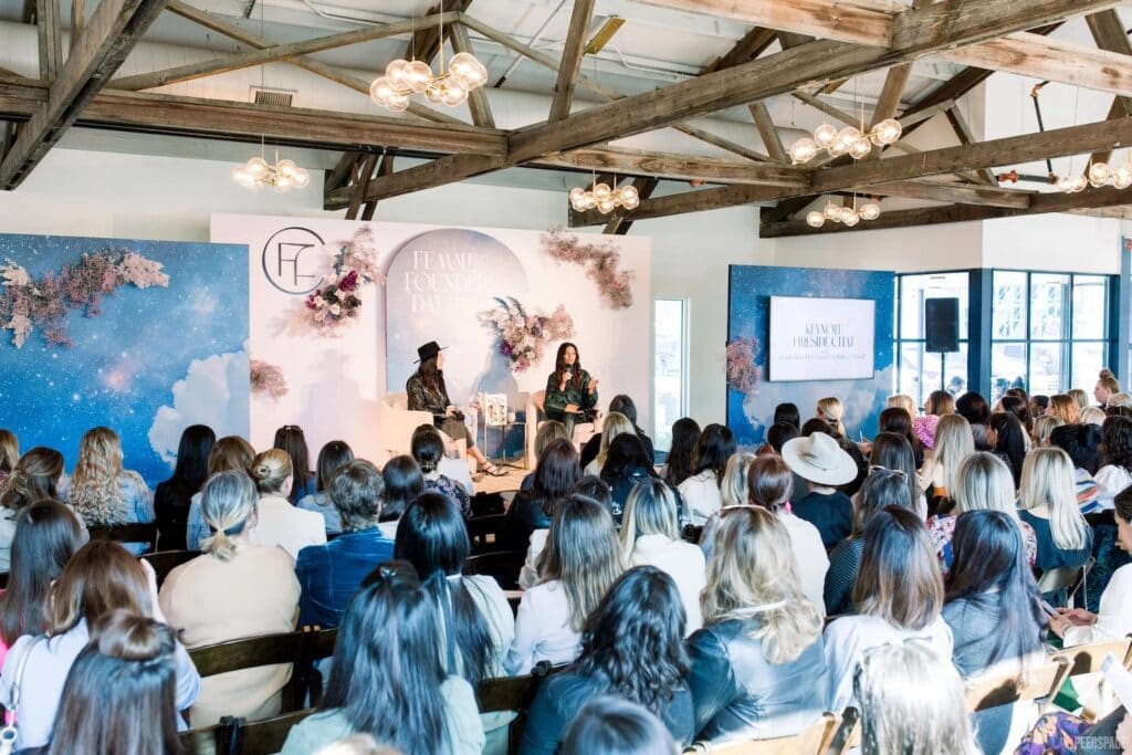 Speakers on stage at an event speak to a room of guests