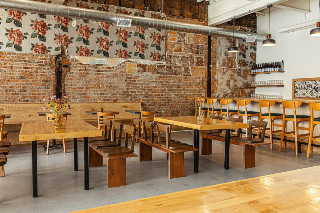 An original, exposed-brick wall sets the tone for a brewery space decorated with wooden banquets and long tables with benches