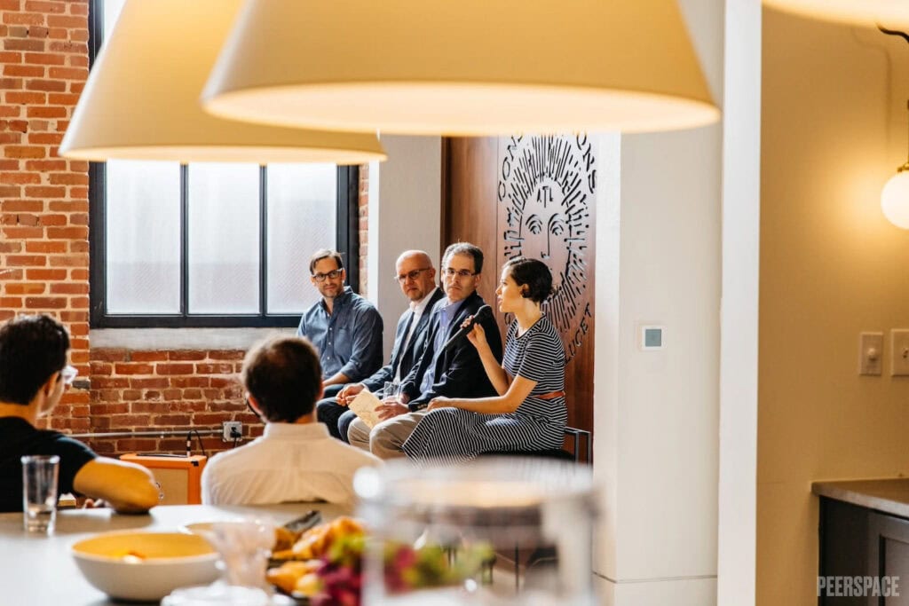 People address a group in an exposed-brick meeting space