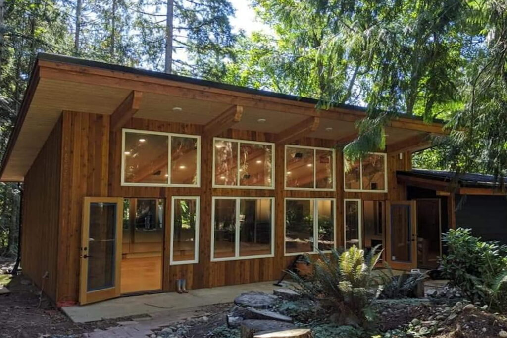 Exterior of a Pacific Northwest-inspired dance studio with cabin-vibes, warm lighting, and a cathedral ceiling nestled in a wooded setting