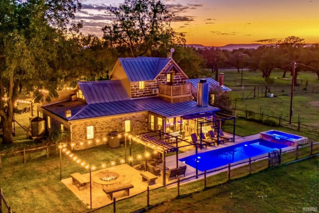 Stone farmhouse with pool and patio is lit by twinkly lights at dusk