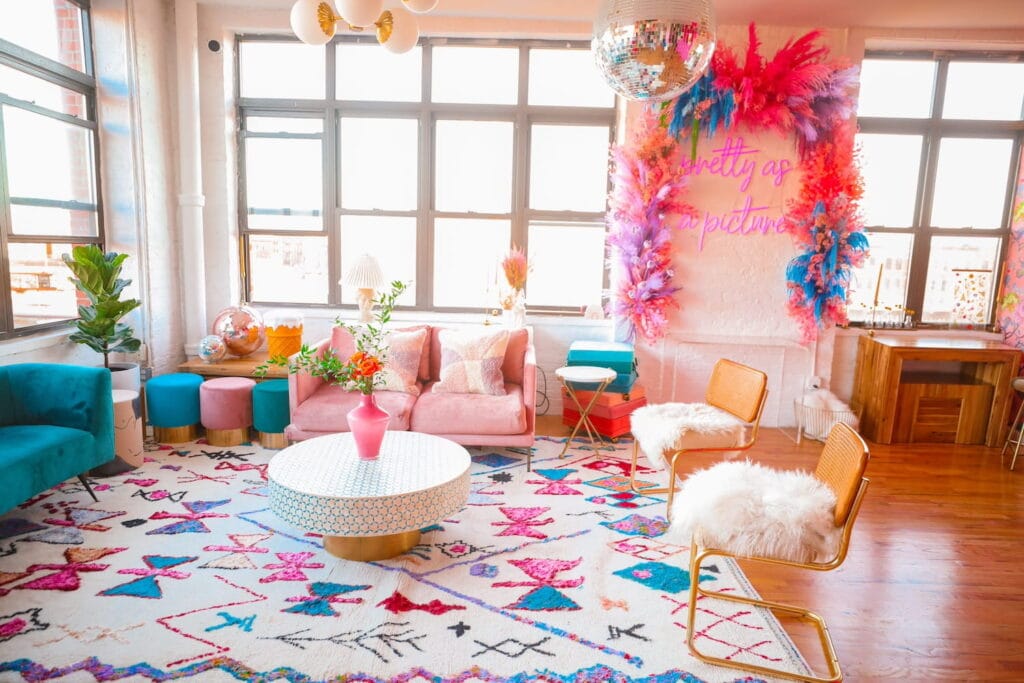 A brightly-decorated, feminine event space with aqua and pink velvet seating and large windows