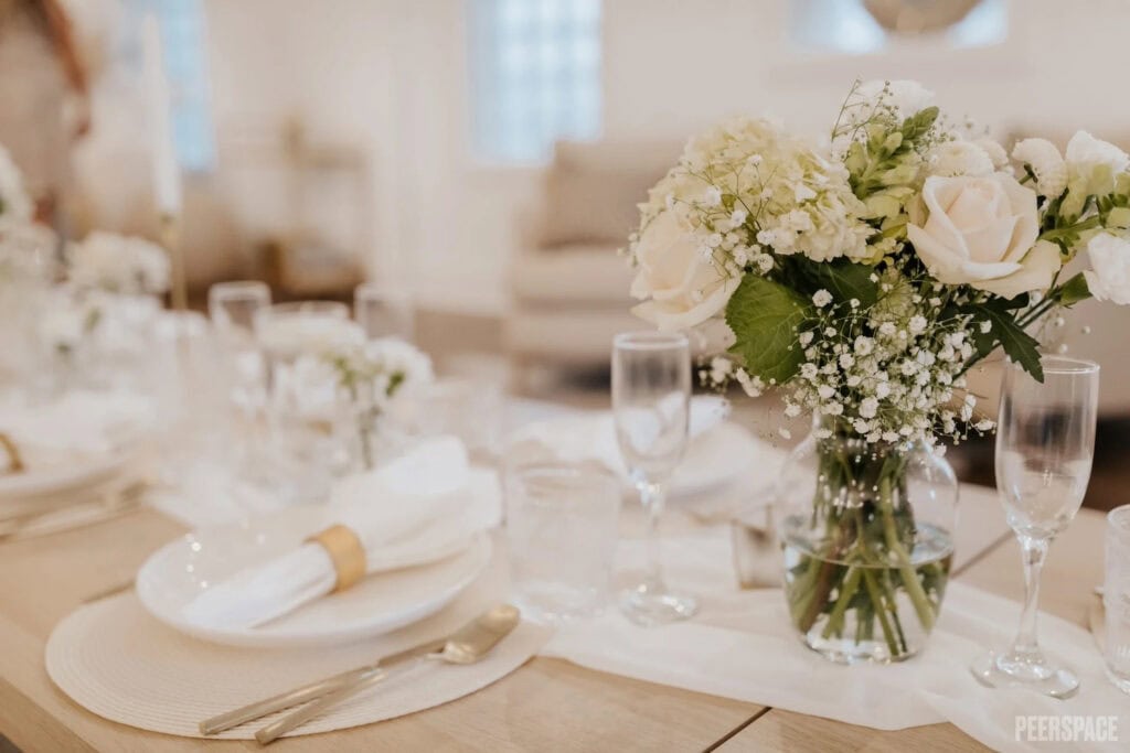 Simple white floral arrangement in a vase atop all-white guest table