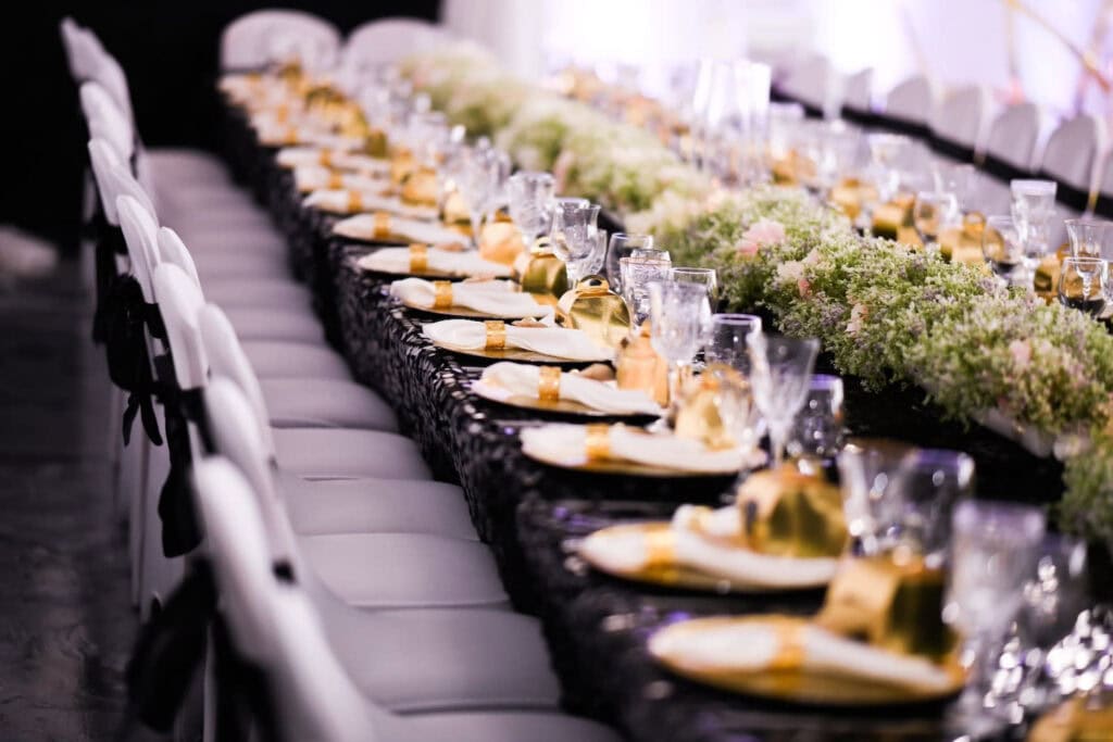 Gold accents punctuate a formal reception table with white cloth chairs, black linens and a continuous, low-lying floral centerpiece
