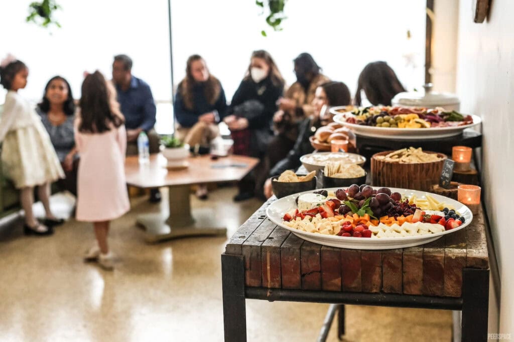 A long table of appetizers and finger foods sits in the foreground as guests sit in the background