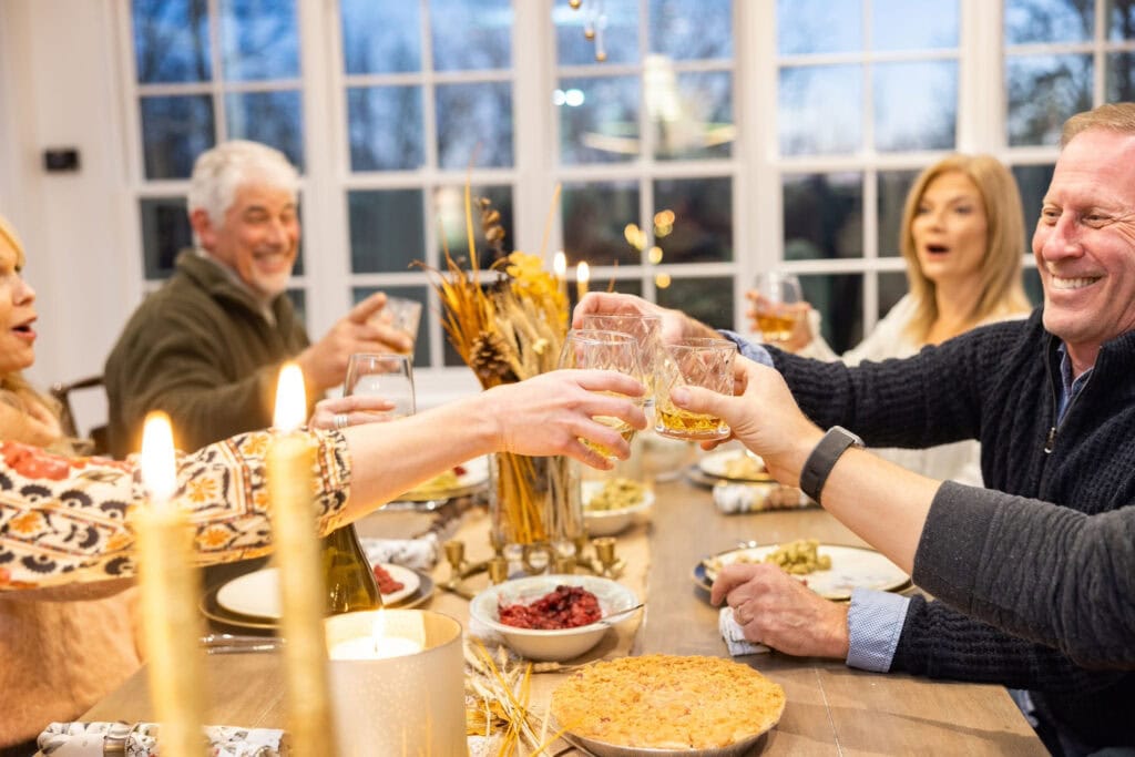 Friends toast around a holiday table with candles lit and fall decor scattered among the dishes
