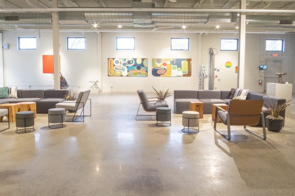 An all-white industrial space with glossy cement floors doubles as an art gallery with cozy seating areas and abstract, brightly-colored art