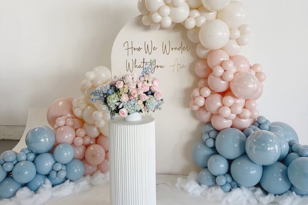 pink and blue balloons and flowers at a gender reveal party