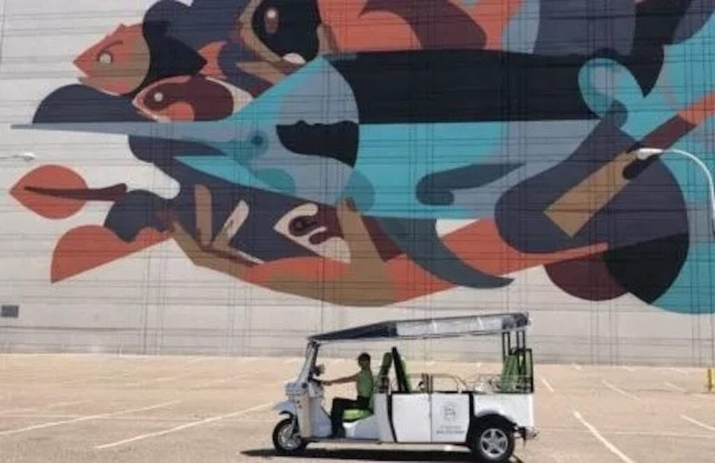 A tuk tuk sits in front of a large mural