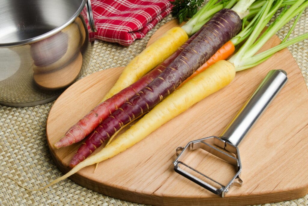 Carrots on cutting board next to vegetable peeler.