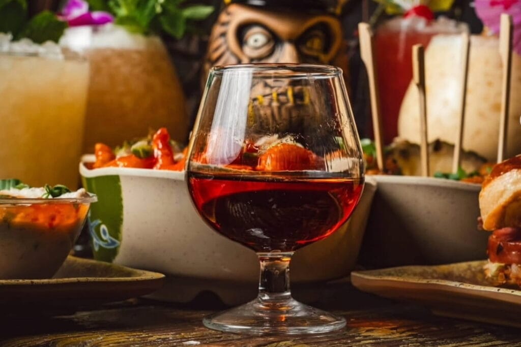 A rich-colored cocktail sits on a table full of tiki decor