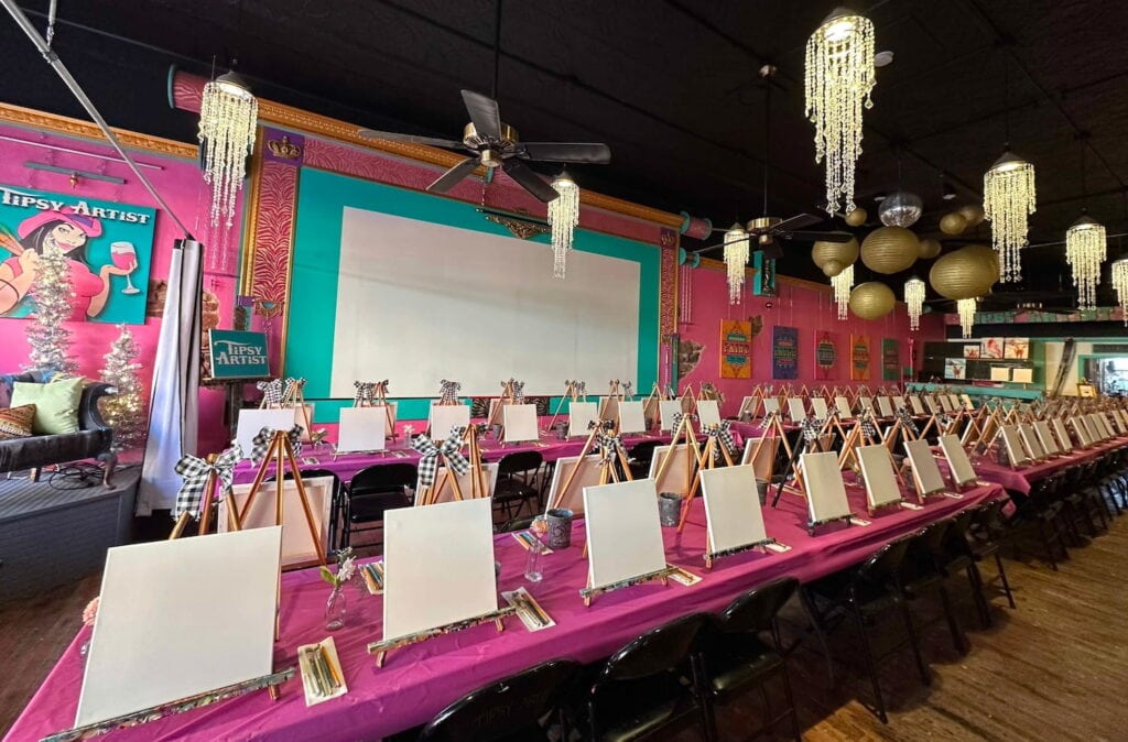 Painting party set up in bright pink room with black ceilings and chandeliers
