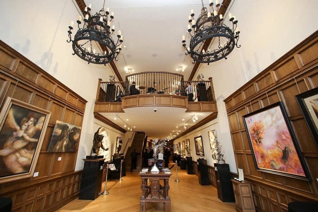 A grand mansion entryway with wooden walls hung with art and statues on pedestals and a band set up on a balcony overlook