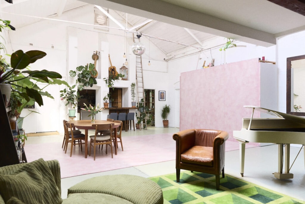 All-white warehouse living space with tall ceilings, plants, and a grand piano complete with disco ball