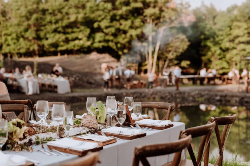 A close up of a rustic banquet table outdoors with wedding festivities happening in background