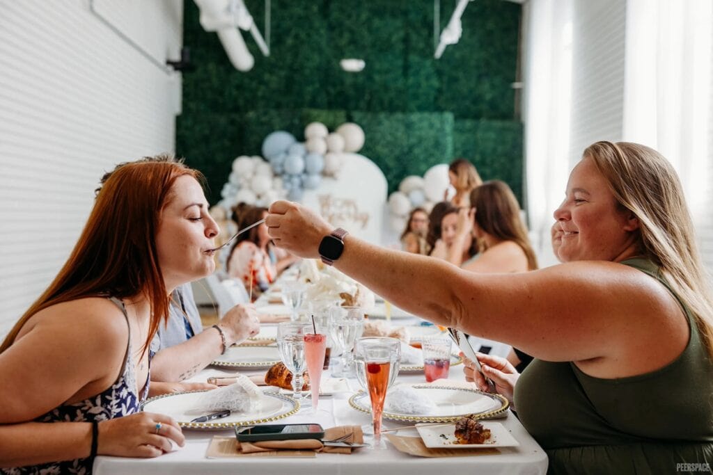 One party guest feeds another from across the table at a baby celebration