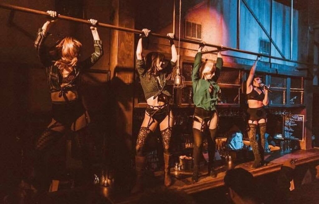 Four women in lingerie dance and sing while standing on a bar in LA