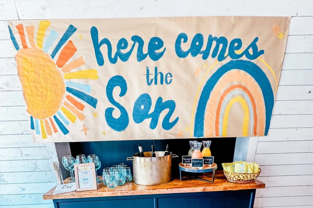 A hand-painted sign that reads Here Comes the Son hangs above a self-serve bar at a baby event