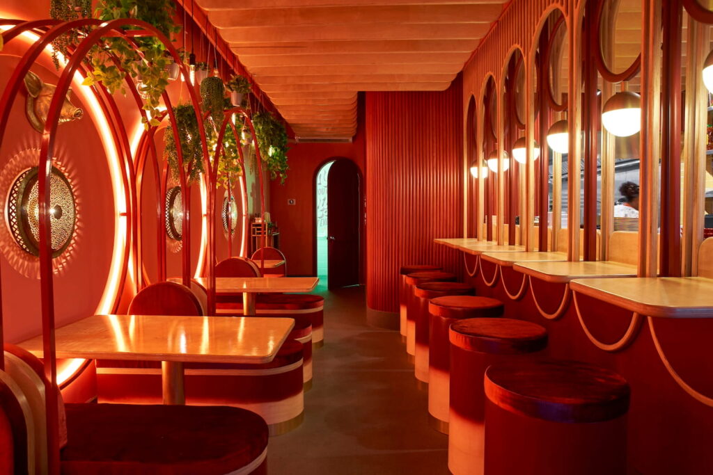 A moody and intimate restaurant space with small tables and a unique bar area, dimly lit by lots of ornate lighting