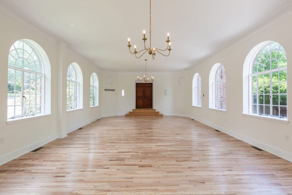 Bright, white event space in a historic hall with large, curved windows and simple chandeliers