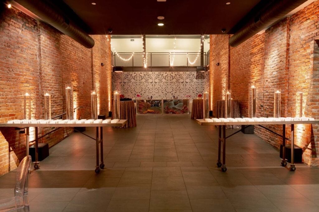 An historic theater turned event space with exposed brick walls is lit by string lights and candles
