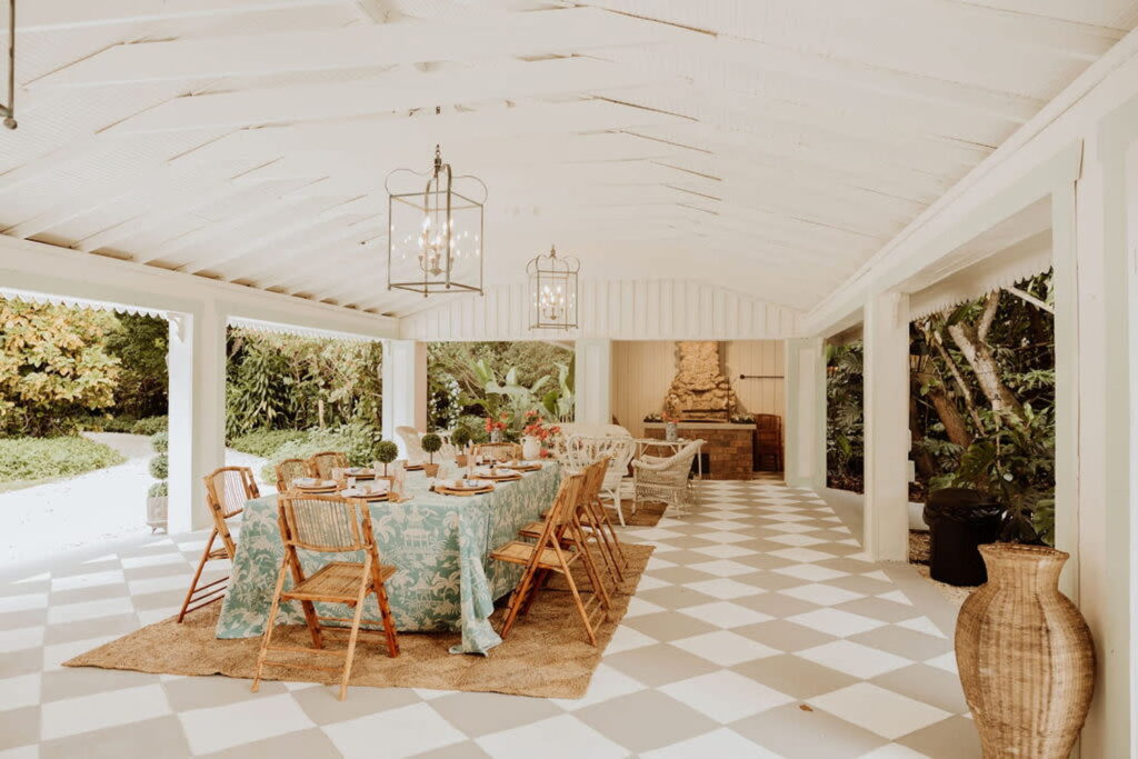 Bamboo chairs surround a long guest table set up for a meal under a large white verandah in the backyard of a Florida home