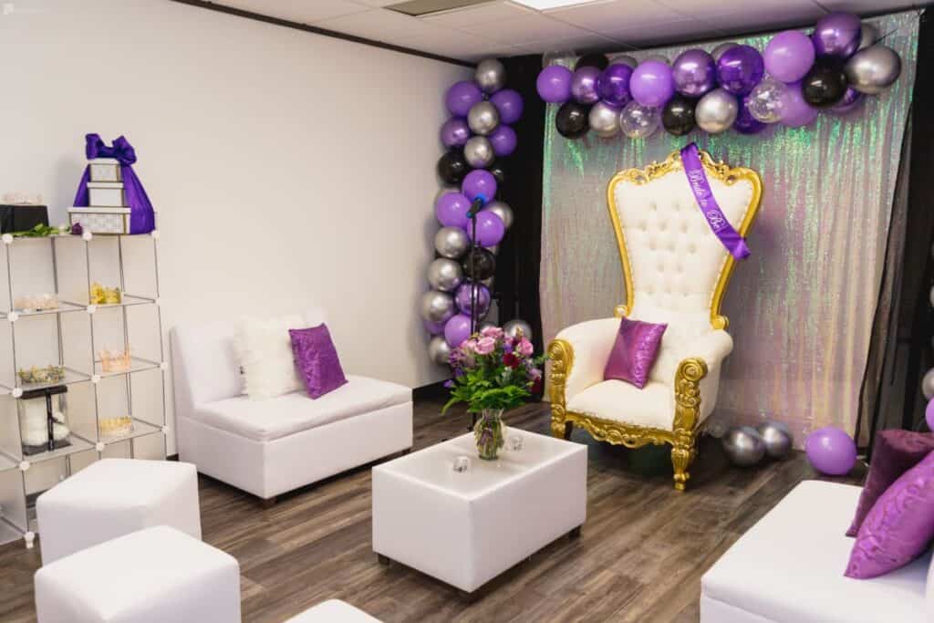 an event space with a white throne and purple balloon arch