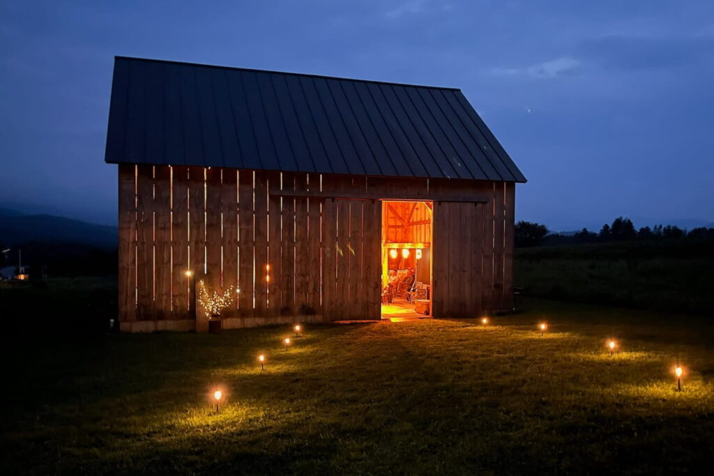 Exterior shot of small barn at night illuminated inside by dim lights and pathway lights leading to doorway