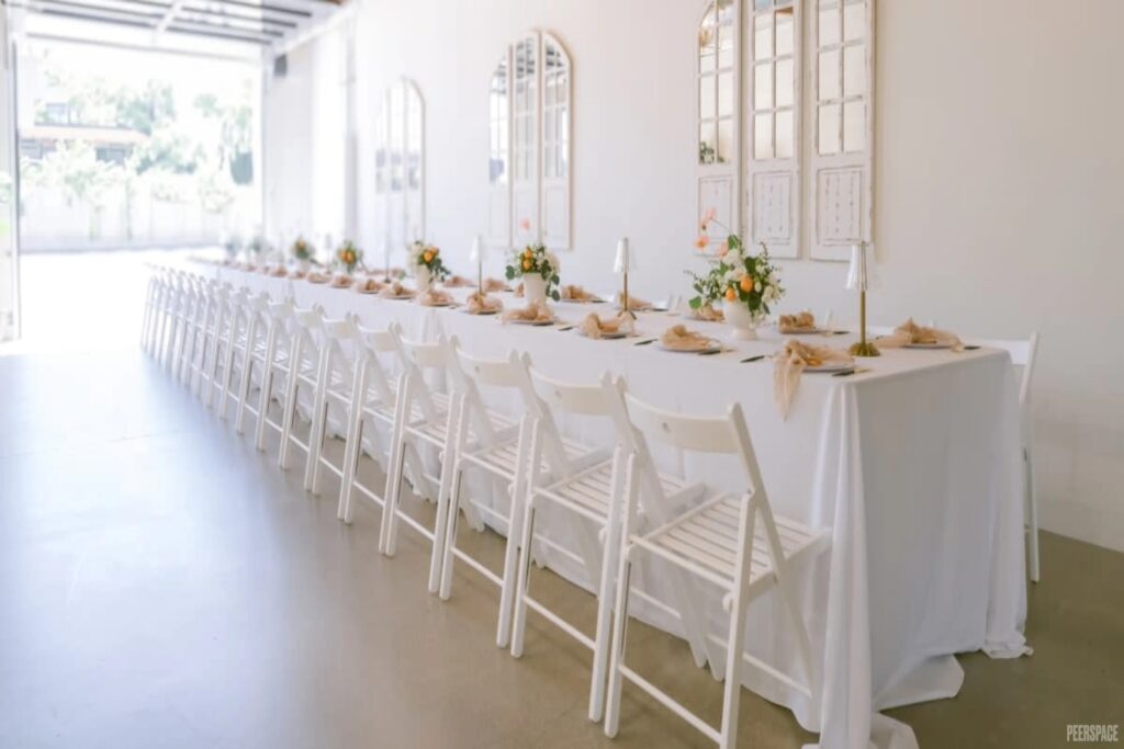 A crisp, white, long table is set and ready for guests with a wide garage door open to the exterior