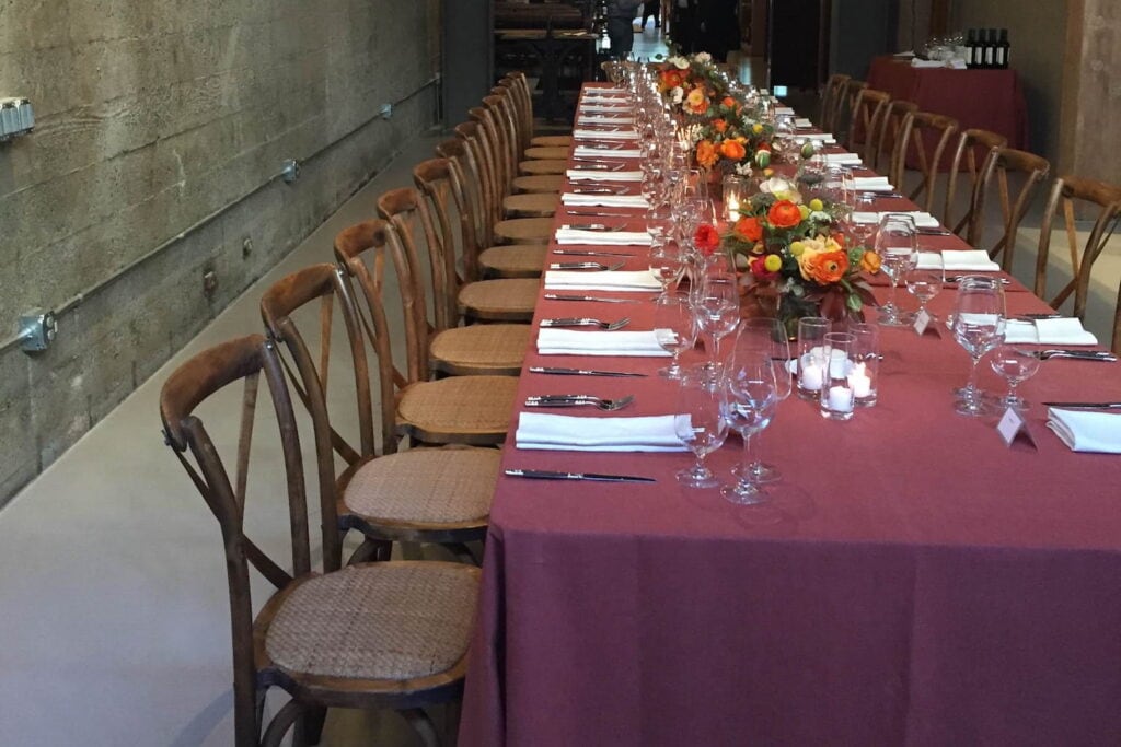 A long dining table dressed in maroon linens in an industrial venue with orange and yellow centerpieces running down the middle