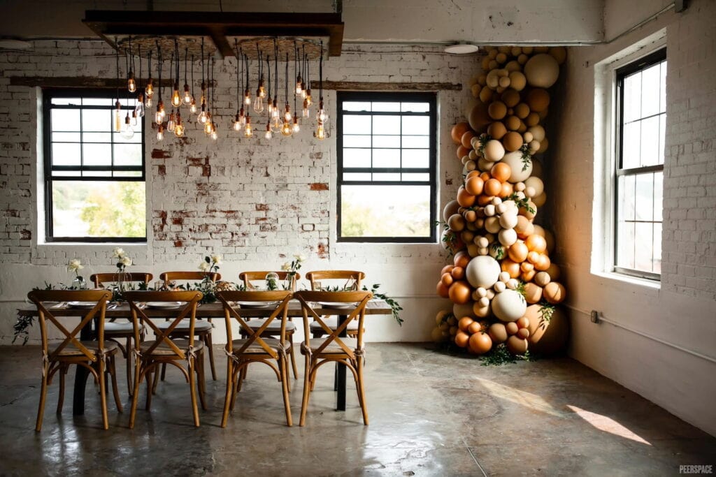 A small table is set in a rustic venue with balloon decor