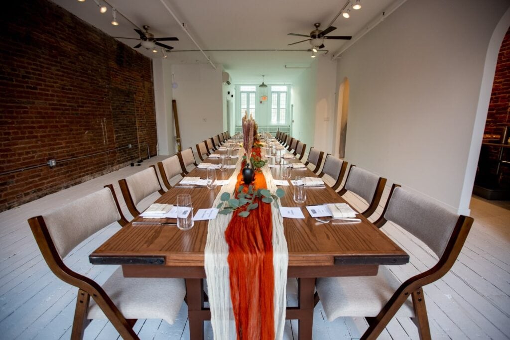 An intimate, narrow space with exposed brick walls and wood-planked floor set for a dinner party