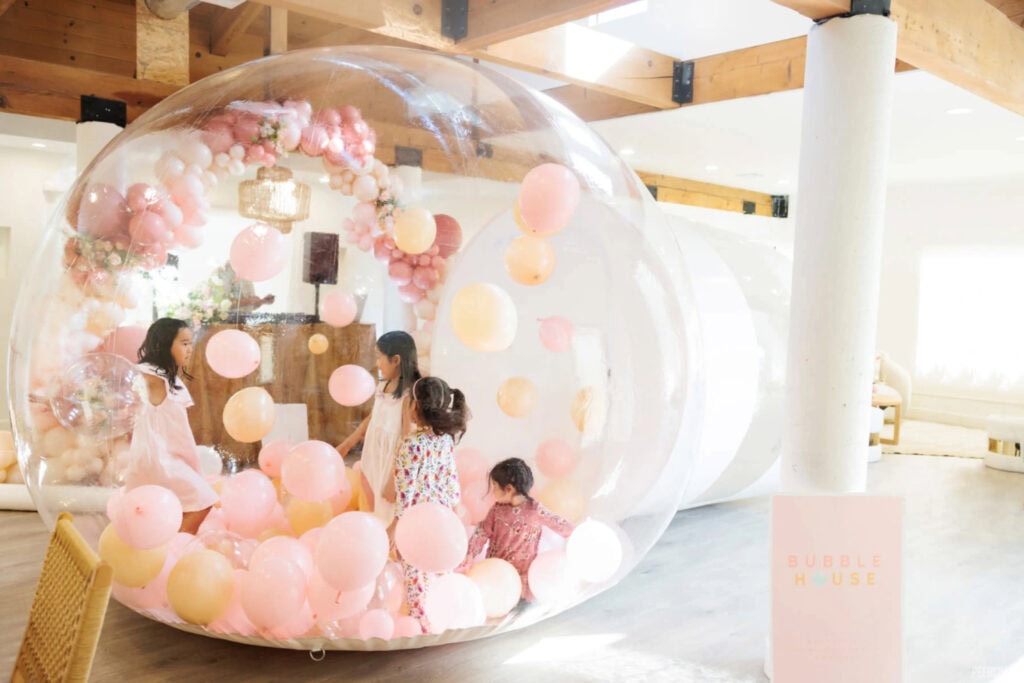 Kids play in bubble house surrounded by pink balloons.