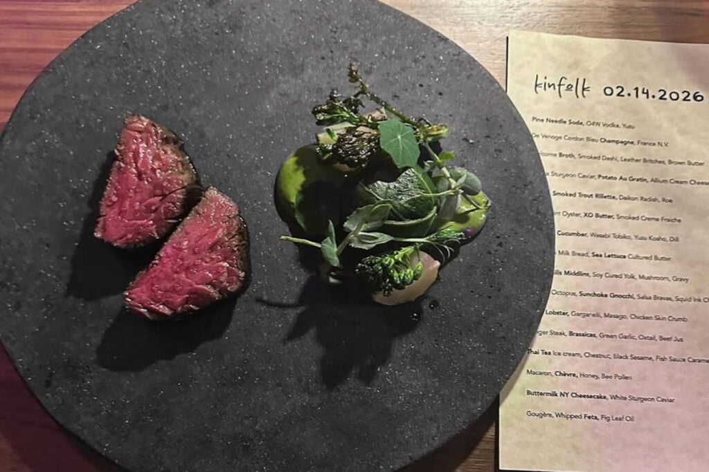 Overhead shot of a small plate of meat and greens next to a menu