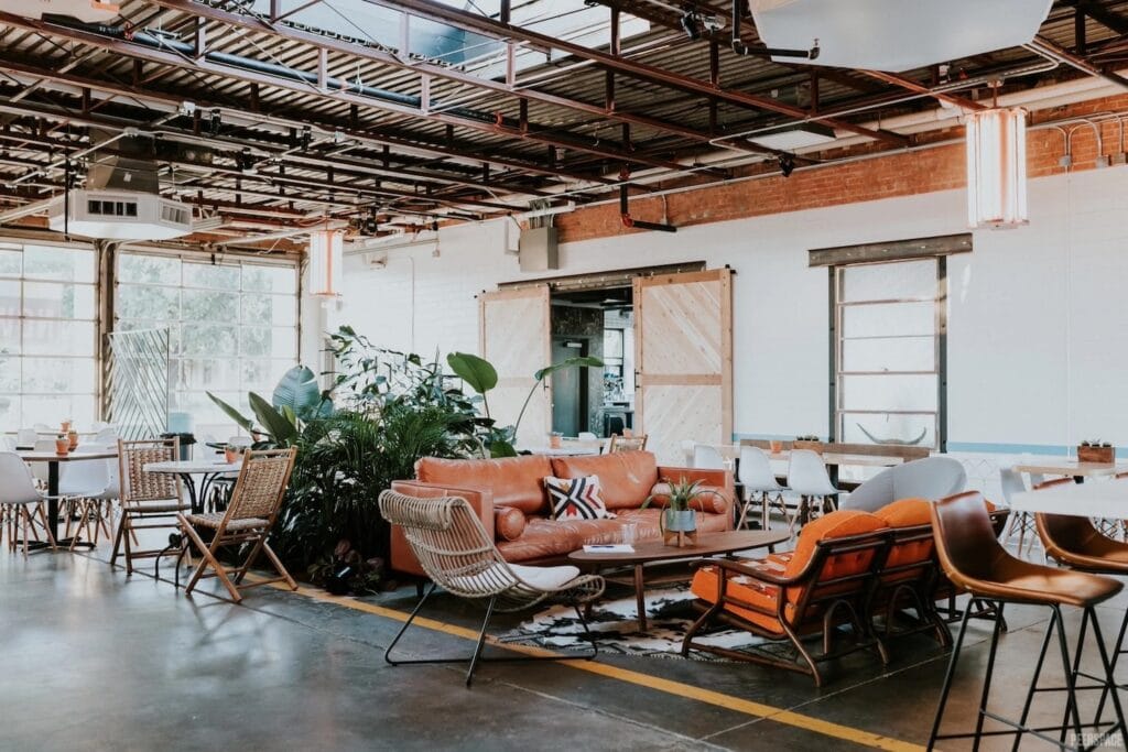 Multi-purpose event space broken out by sections of couches and tables and chairs with high, steel ceilings, large glass doors and other industrial features